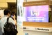 Trade show attendee photographs a transparent MicroLED display illustrating key Micro LED technology benefits like vivid color, high brightness, and seamless transparency for commercial applications