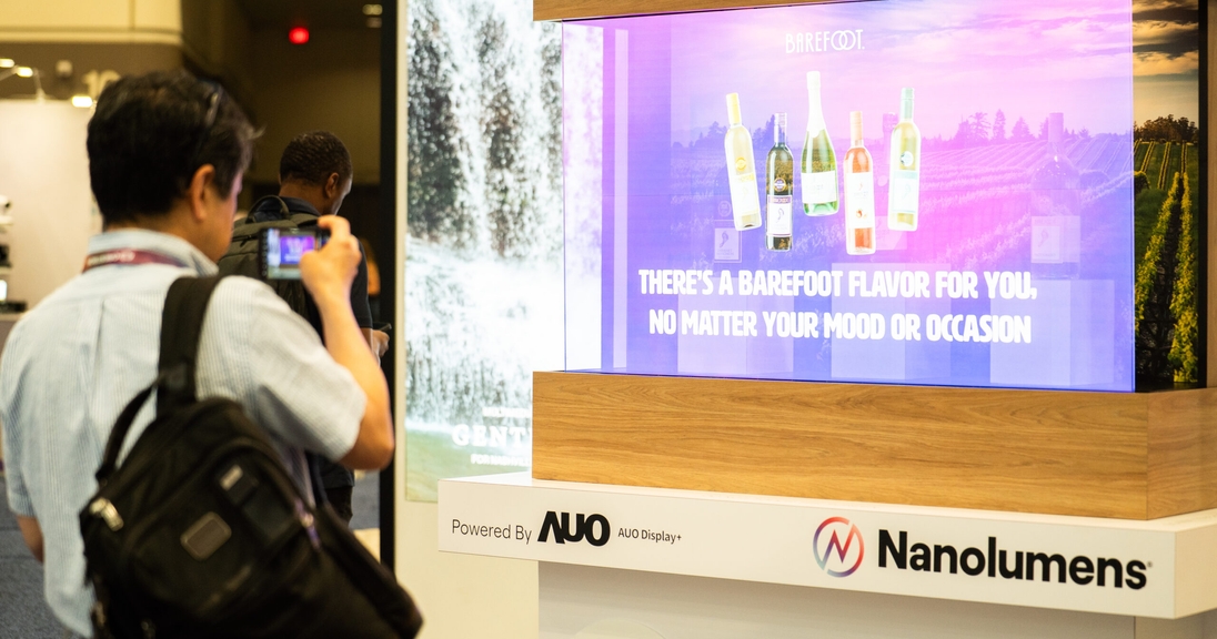 Trade show attendee photographs a transparent MicroLED display illustrating key Micro LED technology benefits like vivid color, high brightness, and seamless transparency for commercial applications